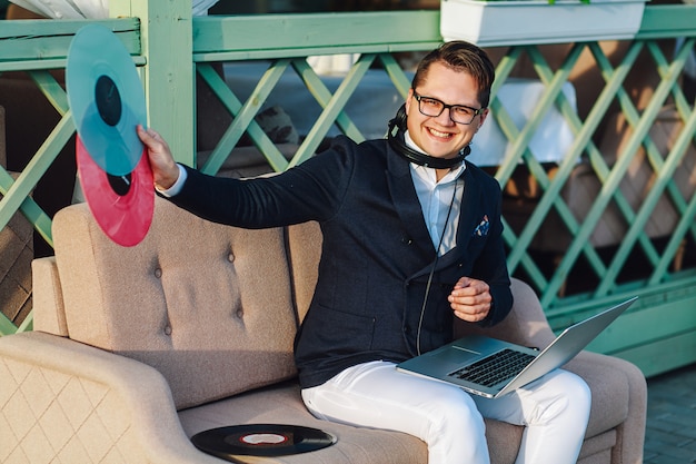 Vrolijke stijlvolle man met een koptelefoon en laptop op zijn kness vinyl plaat buiten te houden