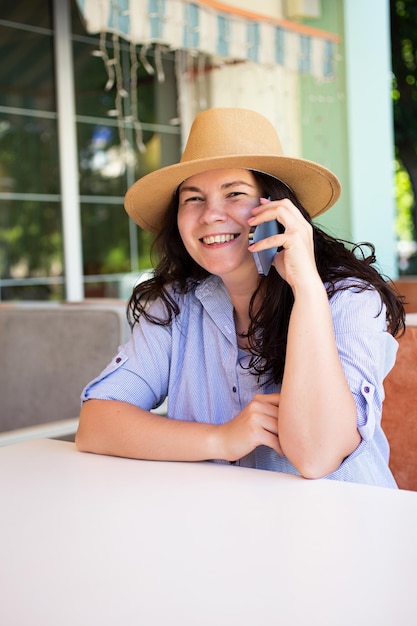 Foto vrolijke stijlvolle vrouw in hoed met smartphone buiten