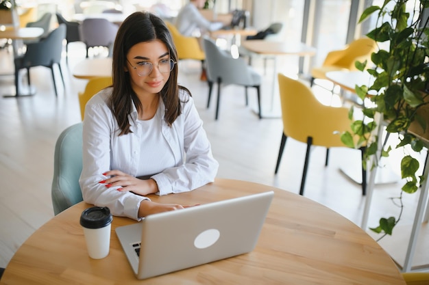 Vrolijke studente die online studeert in café met lege ruimte voor laptop en koptelefoon