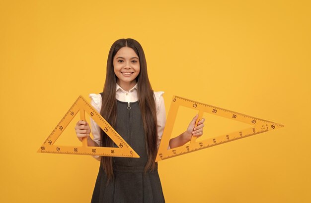 Vrolijke tienermeisje houdt wiskunde driehoek liniaal op school op gele achtergrond onderwijs