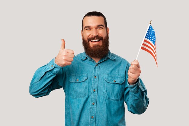 Vrolijke trotse man met blauw shirt houdt een duim omhoog en de vlag van de VS