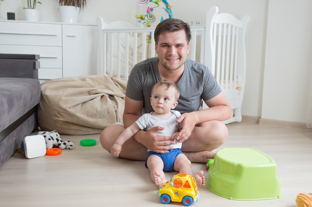 Vrolijke vader die plezier heeft met zijn babyjongen en op de vloer speelt