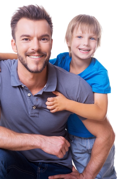 Vrolijke vader en zoon. Gelukkig jongetje dat zijn vader omhelst en glimlacht terwijl ze allebei geïsoleerd op wit staan