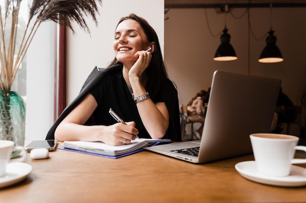 Vrolijke verraste vrouw glimlacht en kijkt naar het bedrag van de inkomensinkomsten salaris en verheugt zich Gelukkig meisje verheugt zich in het winnen en zitten achter laptop in café