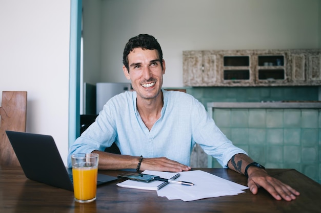 Vrolijke volwassen mannelijke werknemer zittend aan tafel tijdens het werk