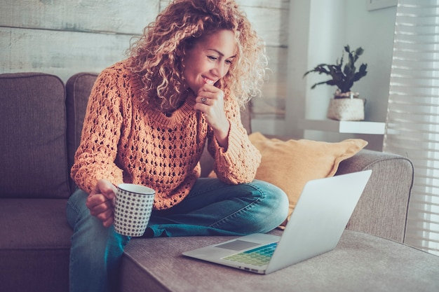 Vrolijke volwassen moderne vrouw gebruikt laptop thuis zittend op de bank glimlachend en genietend van verbinding internettechnologie - concept van online baan vrouwelijke mensen die op internet werken - slim beroepsleven