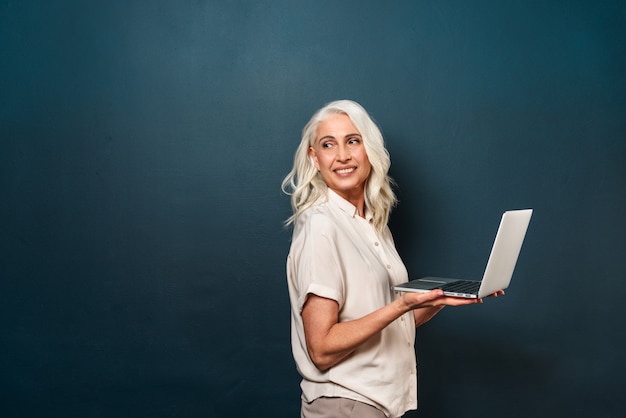 Vrolijke volwassen oude vrouw met laptopcomputer.