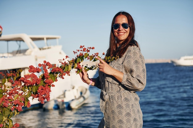 Vrolijke volwassen vrouw die tegen een wit jacht op de zee staat