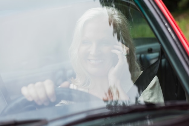 Vrolijke volwassen vrouw op de telefoon die rode cabriolet drijft