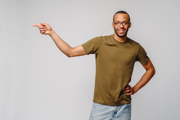 Vrolijke vriendelijke Afro-Amerikaanse jongeman in groen t-shirt wijzend met de vinger op lege ruimte