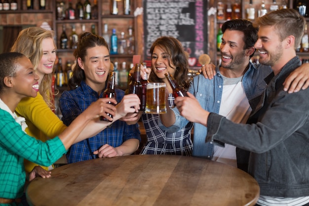 Vrolijke vrienden die bierglazen en flessen roosteren