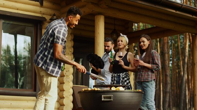 Vrolijke vrienden die rusten op een grillfeestje buitenshuis Kerels rammelende glazen