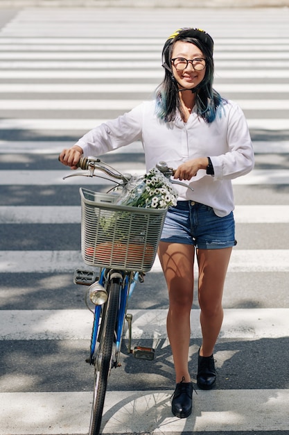 Vrolijke vrij jonge Chinese vrouw met fiets die weg in stad kruist