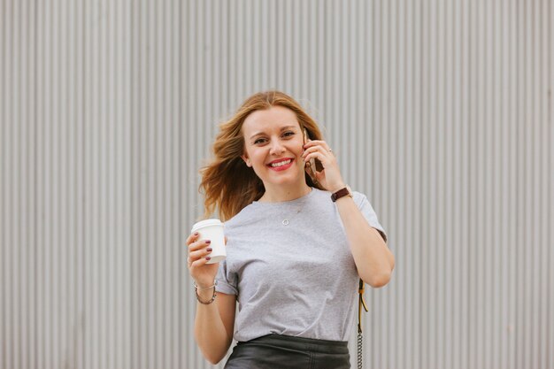 Vrolijke vrouw die aan haar telefoon spreekt terwijl het drinken van koffie