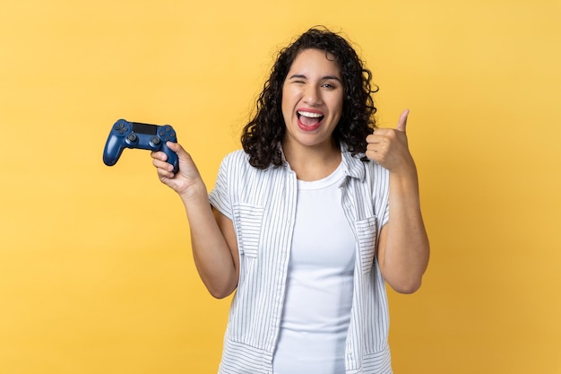 Vrolijke vrouw die joystick in handen houdt en duim laat zien, speelt graag spelletjes op joypad