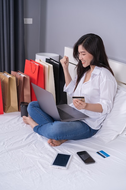 Vrolijke vrouw die laptop computer met online aan het winkelen op bed met behulp van