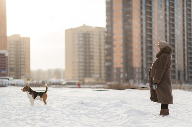 Vrolijke vrouw die met een hond op een weide in de winter loopt