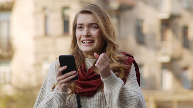 Vrolijke vrouw die met telefoon springt Opgewonden meisje dat mobiel op straat kijkt