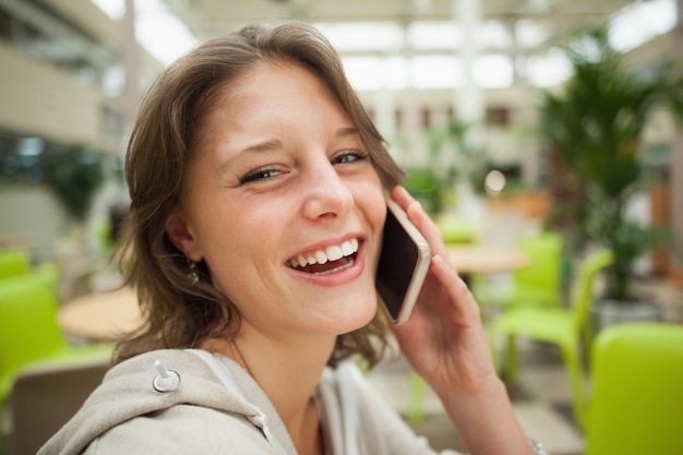 Vrolijke vrouw die mobiele telefoon in de cafetaria met behulp van