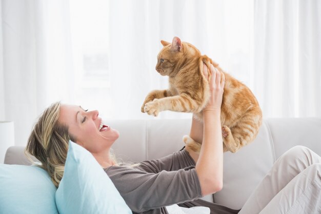 Vrolijke vrouw die op bank ligt die een gringer kat houdt