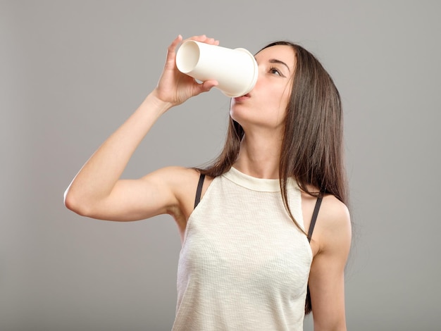 Vrolijke vrouw die 's ochtends koffie drinkt geïsoleerd op een grijze achtergrond