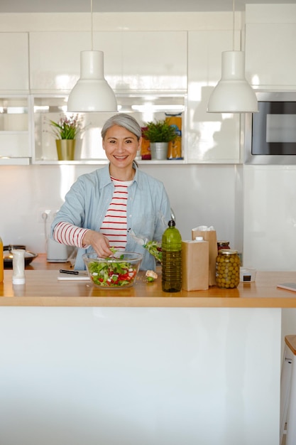 Vrolijke vrouw die thuis groentesalade maakt