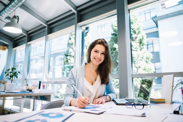 Foto vrolijke vrouw doet papierwerk op laptop