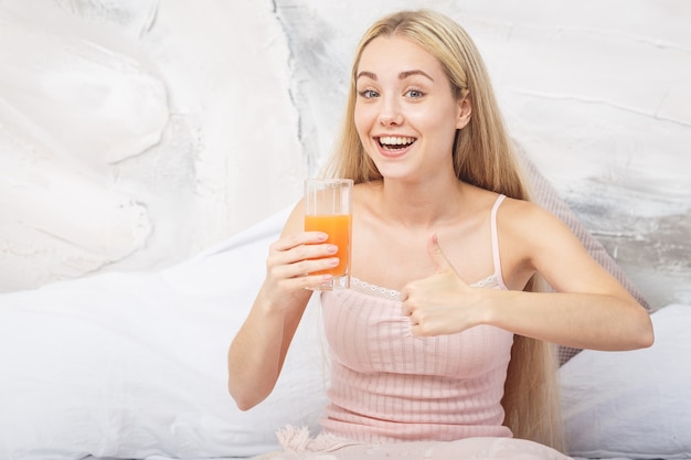 Vrolijke vrouw drinken een jus d'orange zittend op haar bed thuis