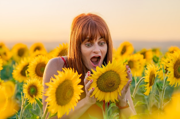 Vrolijke vrouw genieten van de dag in een zonnebloemveld en op zoek naar een zonnebloem.