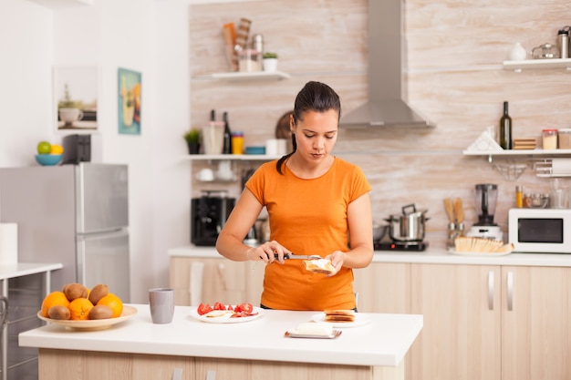 Vrolijke vrouw in de ochtend die boter op geroosterd brood uitspreidt.