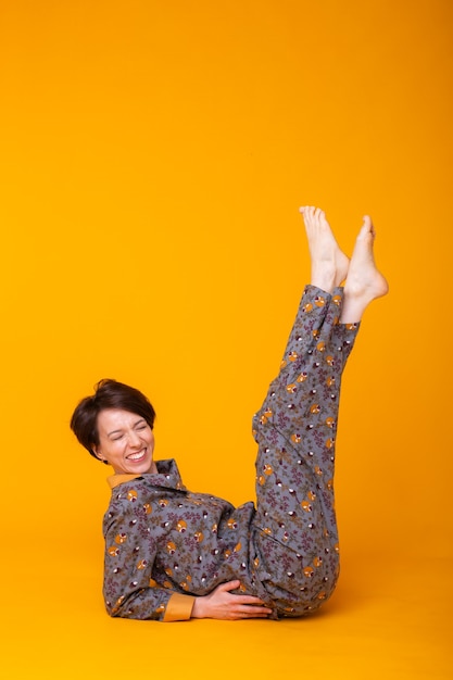 Vrolijke vrouw in huiskleding pyjama in gele muur
