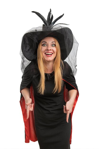 Foto vrolijke vrouw in zwarte hekshoed en jurk wijst naar beneden halloween feest witte achtergrond jonge heks verticaal frame