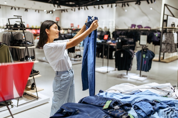 Vrolijke vrouw jeans in kledingwinkel kiezen