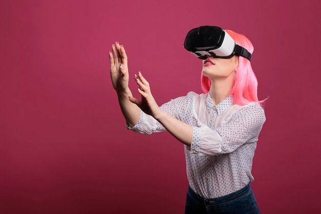 Vrolijke vrouw met behulp van virtual reality-bril met 3D-visie, interactieve visuele simulatie op vr-bril. Elektronische futuristische ervaring met verbeterde technische innovatie op roze achtergrond.