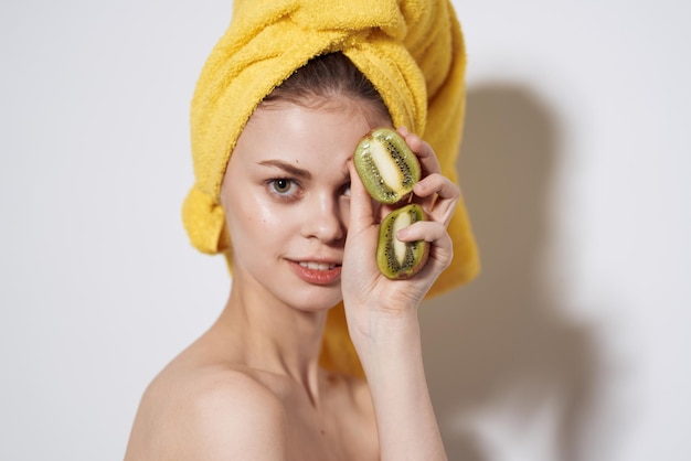 Vrolijke vrouw met blote schouders QIWI in handen met een handdoek op haar hoofd bijgesneden weergave lichte achtergrond