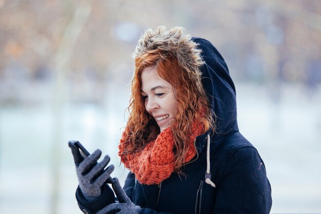 Vrolijke vrouw met een jas met behulp van haar mobiele telefoon