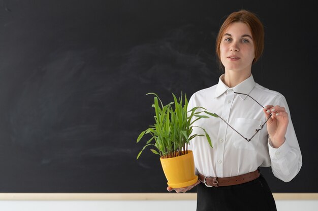 Vrolijke vrouw met een plant in de buurt van een schoolbord