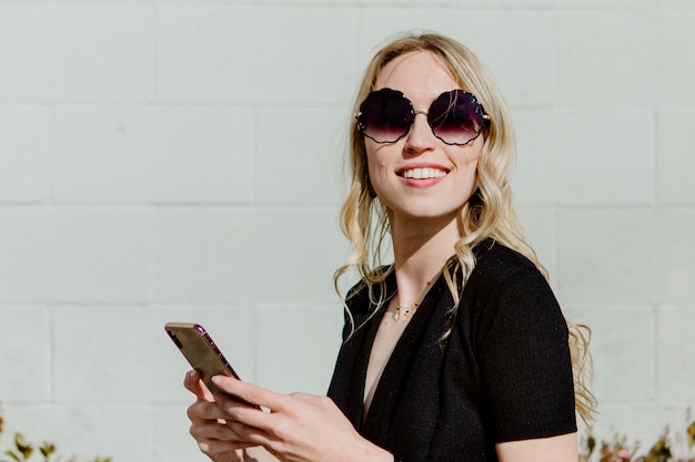 Vrolijke vrouw met een zonnebril sms't op haar telefoon