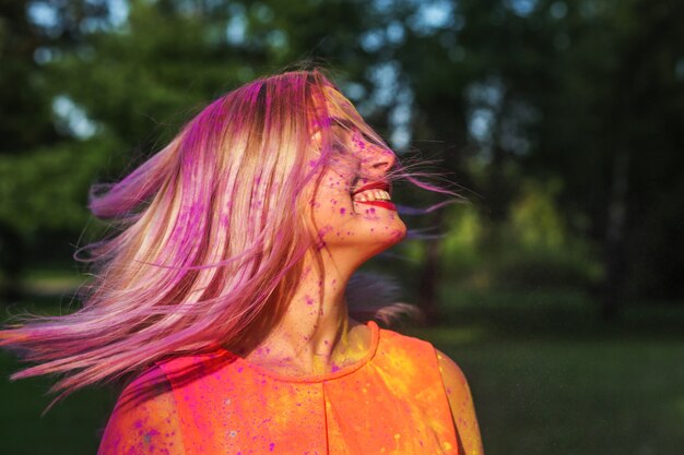 Vrolijke vrouw met haar in beweging spelen met kleurrijke droge verf