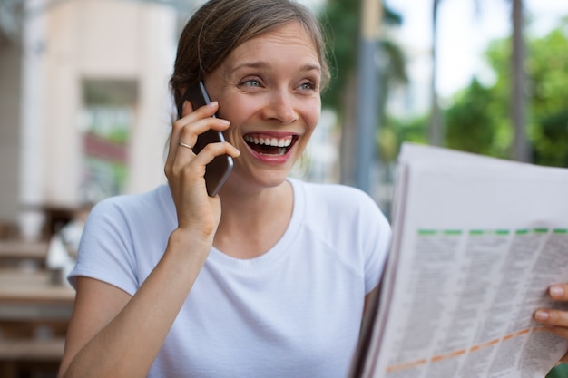 Vrolijke Vrouw met Krant die op Telefoon uitnodigt