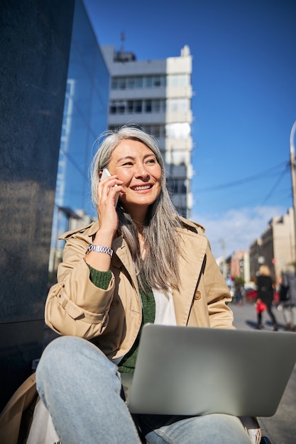 Vrolijke vrouw met laptop die buiten telefoongesprek voert