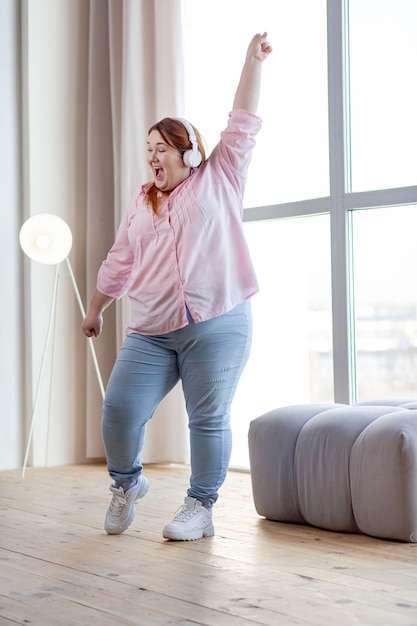 Vrolijke vrouw met overgewicht die op muziek danst terwijl ze thuis veel plezier heeft