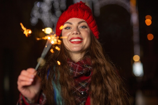 Vrolijke vrouw met rode hoed die 's avonds plezier heeft met fonkelende lichten buiten