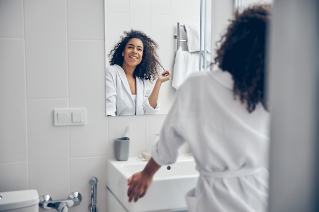 Vrolijke vrouw speelt met een lok van haar krullend haar voor de spiegel