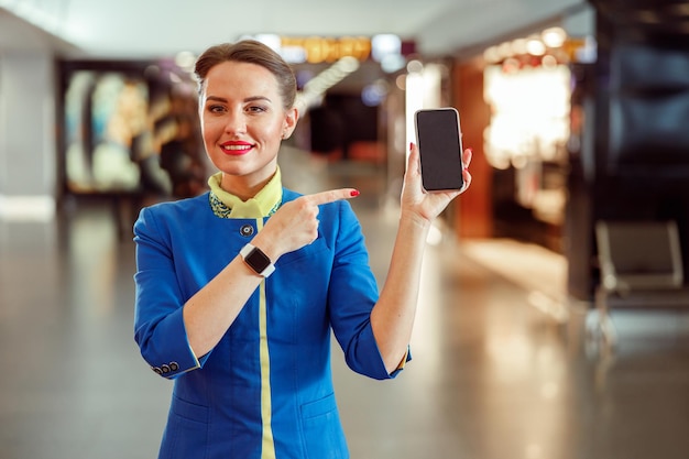 Vrolijke vrouw stewardess wijzend op smartphone op luchthaven