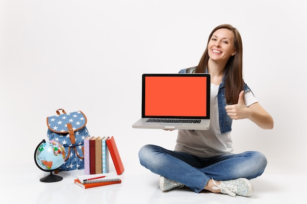 Vrolijke vrouw student houdt laptop pc-computer vast met een leeg zwart leeg scherm met duim omhoog in de buurt van de wereld, rugzak schoolboeken geïsoleerd