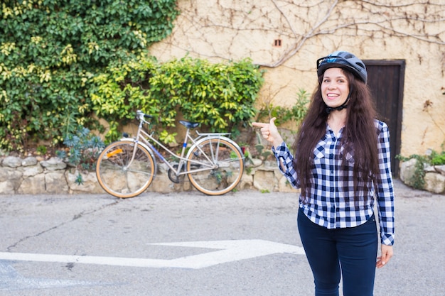 Vrolijke vrouw vertegenwoordigt een fiets op de muursteeg