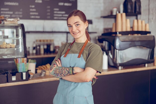 Vrolijke vrouwelijke barista in schort die in koffiehuis staat