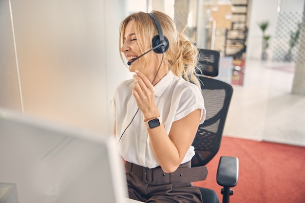 Vrolijke vrouwelijke klantenservicemedewerker zit aan tafel met computer en lacht