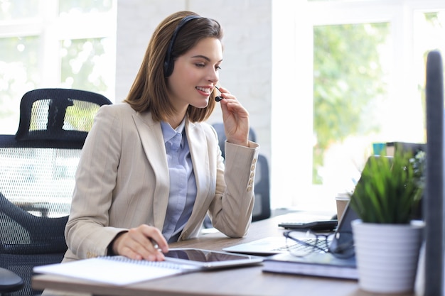 Vrolijke vrouwelijke manager zit aan een bureau en voert zakelijke taken uit met behulp van een draadloze verbinding op digitale gadgets